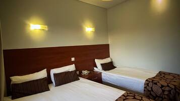 Quarto de hotel com duas camas, cada uma com cabeceira de madeira e roupa de cama branca. Há duas luminárias fixadas no teto.