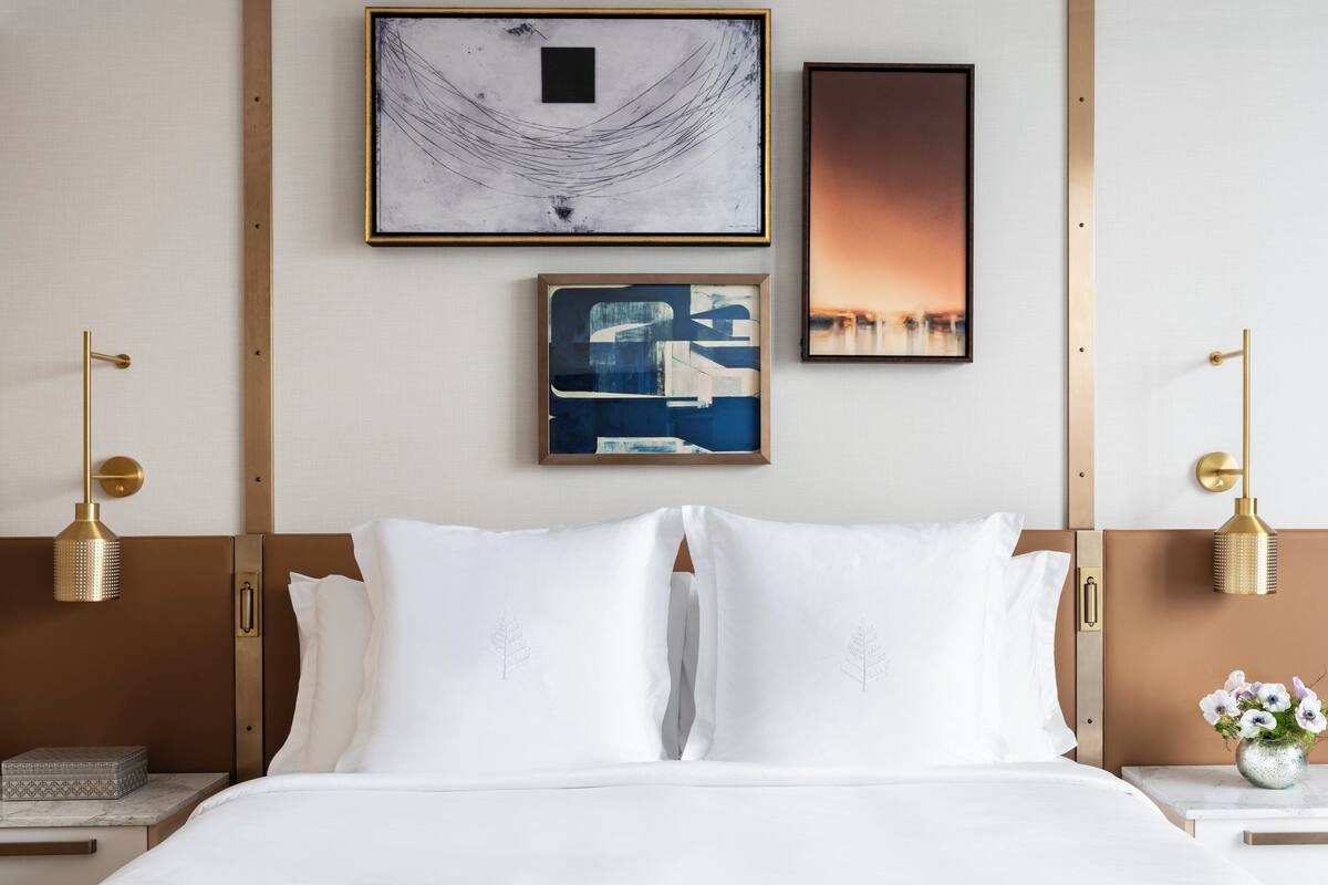 Een hotelkamer met een bed, twee wandlampen en drie kunstwerken in lijsten.