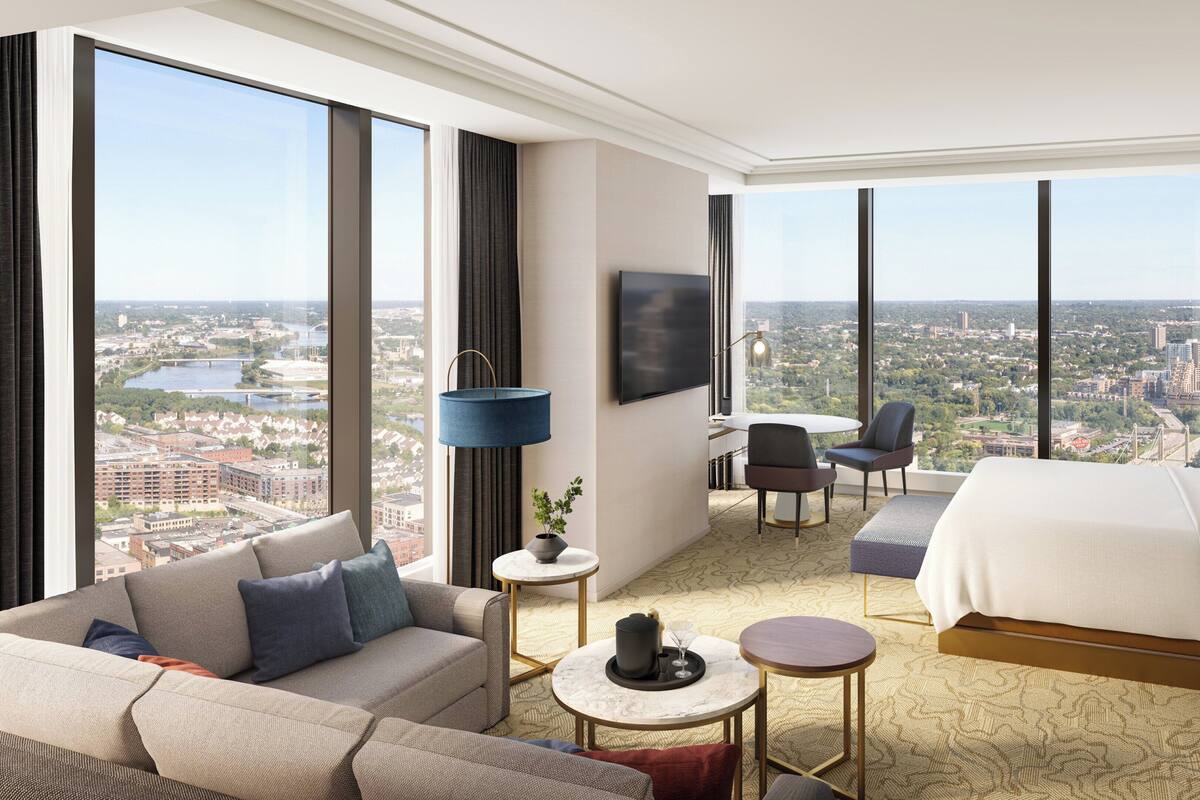 Een moderne hotelkamer met een groot bed, een bank, een eettafel en een televisie. De kamer heeft grote ramen met uitzicht op de stad.