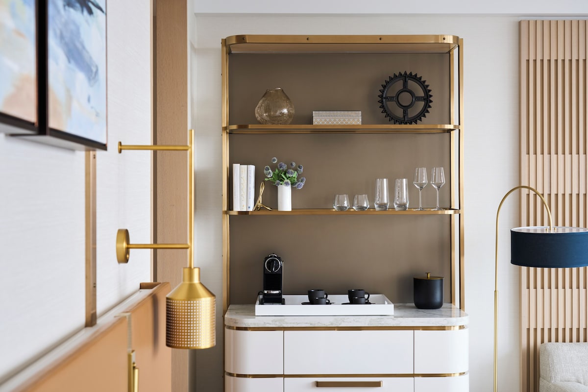 Une cuisine moderne aux couleurs blanc et or, dotée d’un four encastré, d’une machine à café et d’un vase décoratif posé sur le plan de travail.