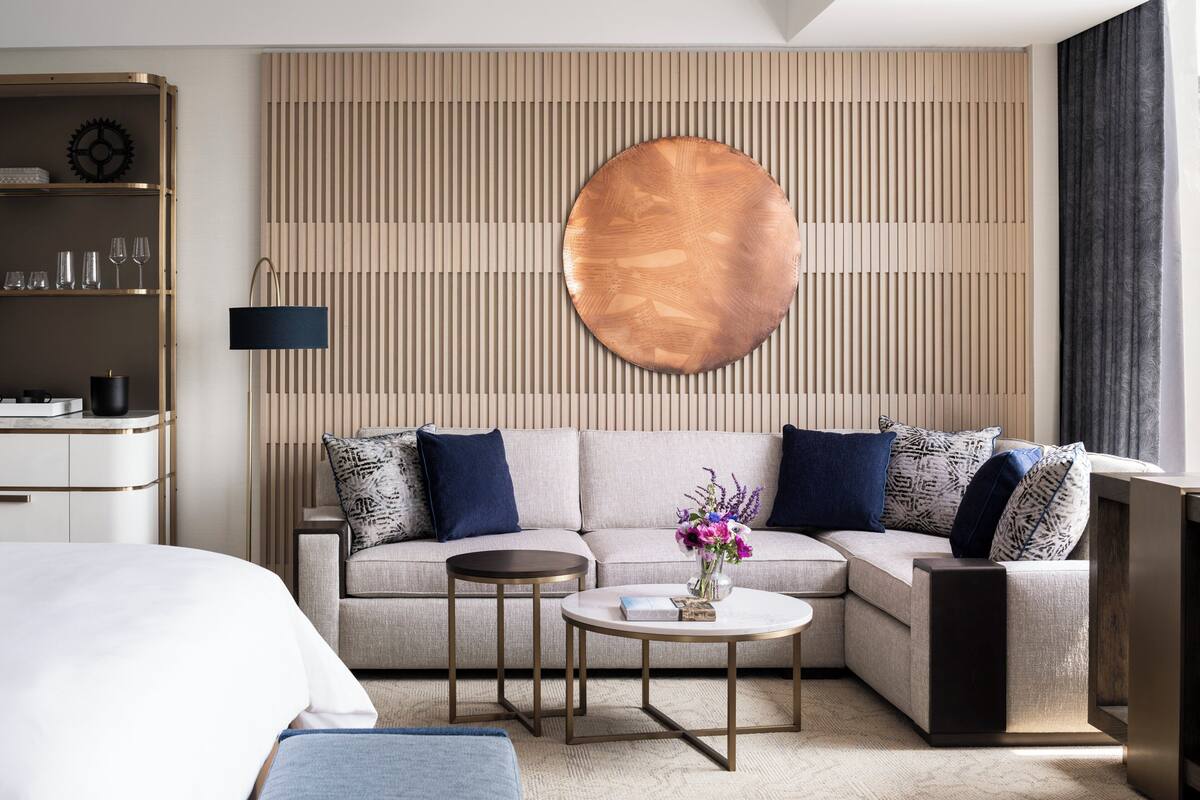 Een moderne hotelkamer met een hoekbank, een ronde salontafel, een nachtkastje en een kledingkast.