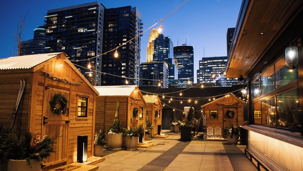 A wooden building with a front porch, potted plants, and string lights.