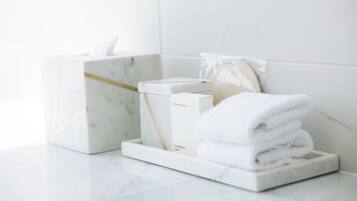 A bathroom with a marble sink, a white towel stack, and a shower cap on a marble tray.