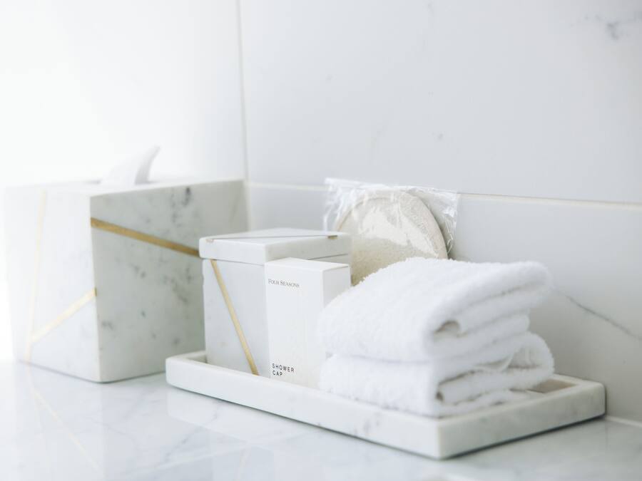 A bathroom with a marble sink, a white towel stack, and a shower cap on a marble tray.