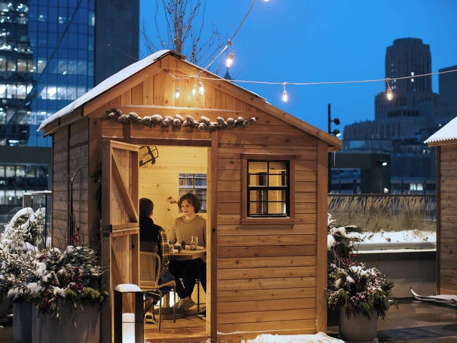 Une cabane en bois avec un porche, deux personnes assises à l’intérieur et de la neige à l’extérieur.