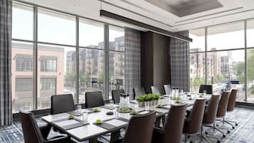 A conference room with a large table, chairs, and a view of buildings through large windows.