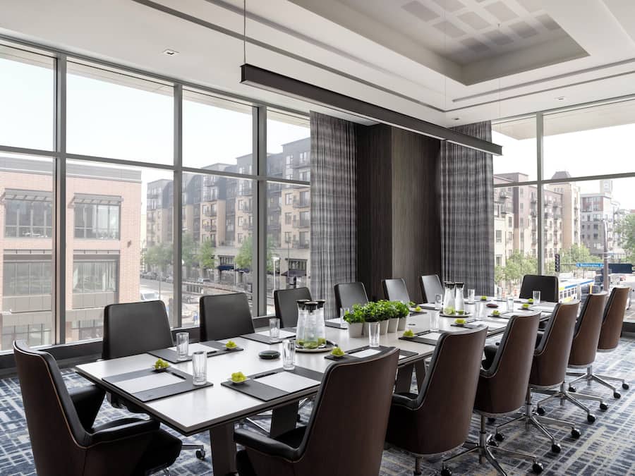 A conference room with a large table, chairs, and a view of buildings through large windows.