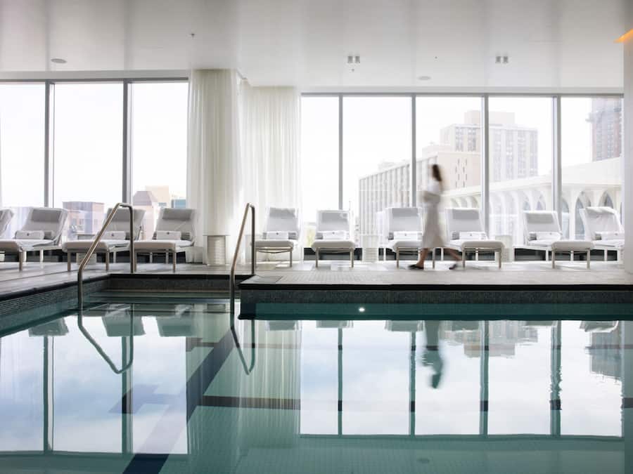 A swimming pool with lounge chairs and a view of buildings through large windows.