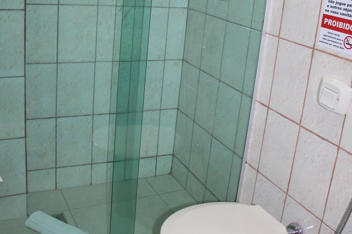 Une salle de bain avec une douche à parois de verre, des toilettes et une poubelle bleue.