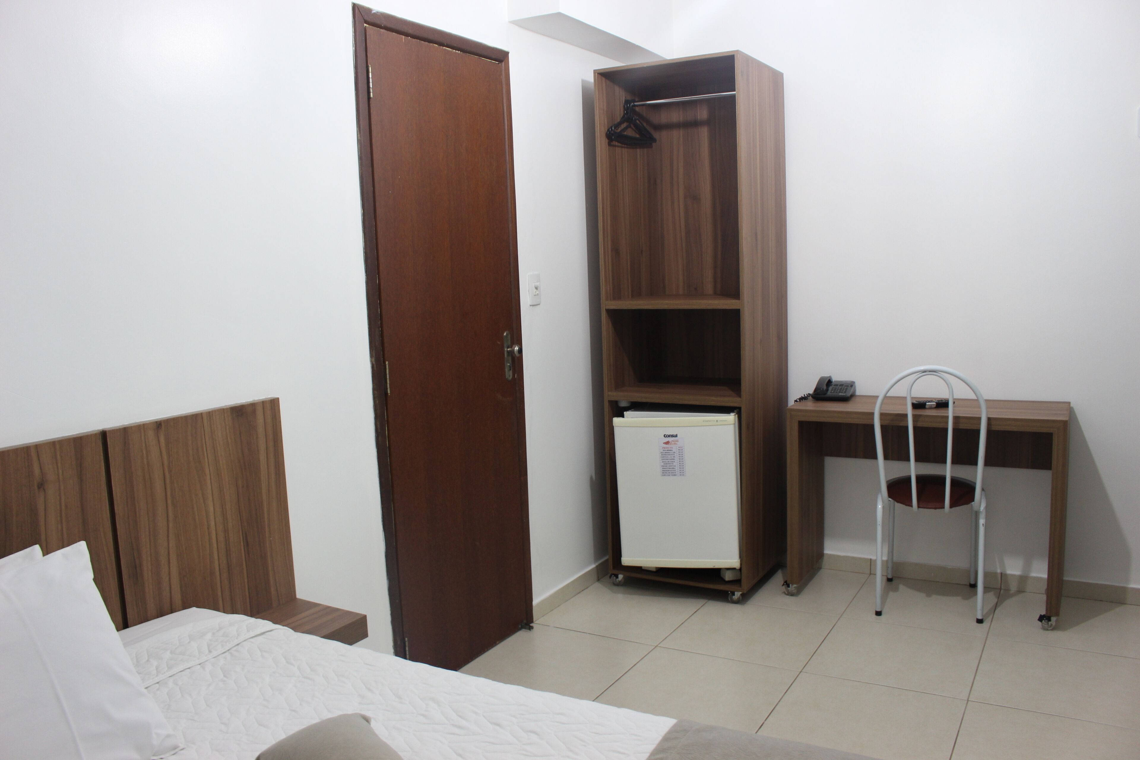 Un dormitorio con una cama de madera, un armario, un escritorio con silla y un refrigerador pequeño.