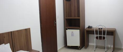 Un dormitorio con una cama de madera, un armario, un escritorio con silla y un refrigerador pequeño.