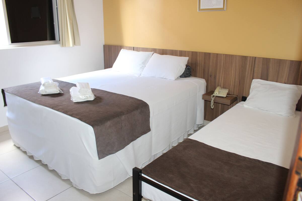 Une chambre d’hôtel avec deux lits, un téléphone sur la table de chevet et une fenêtre avec des rideaux.