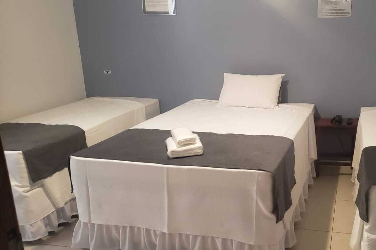 Une chambre d’hôtel avec deux lits simples, une petite table sur laquelle est posée une serviette pliée, et une table de chevet avec une tasse et un livre.