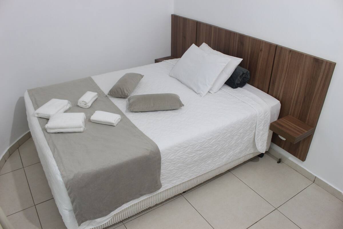 Un lit bien fait, avec une couette blanche, un plaid gris et plusieurs oreillers.