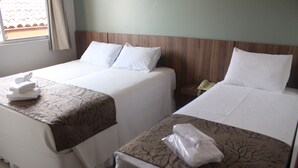 Two beds with white linens and brown tree-patterned bedspreads, a bedside table with a telephone, and a window with curtains.