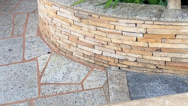 A stone planter with large green plants, a curved stone wall, and a tiled floor.