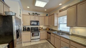 Una cocina moderna con armarios de madera, electrodomésticos de acero inoxidable, microondas, estufa y un lavamanos.
