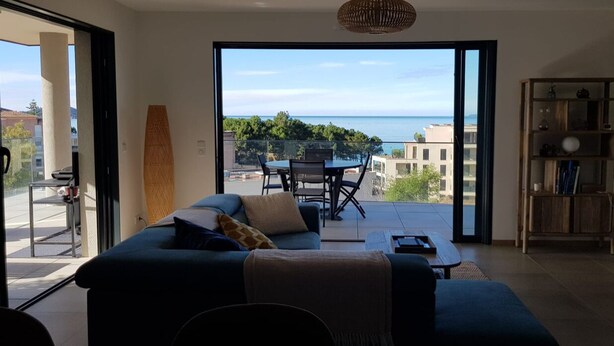 A living room with a sofa, a coffee table, and a view of the sea through a large window. - 4-6 PERSON APARTMENT (Albitreccia)