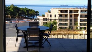 A balcony with a round table and chairs, overlooking a coastal area with buildings and trees. - 4-6 PERSON APARTMENT (Albitreccia)