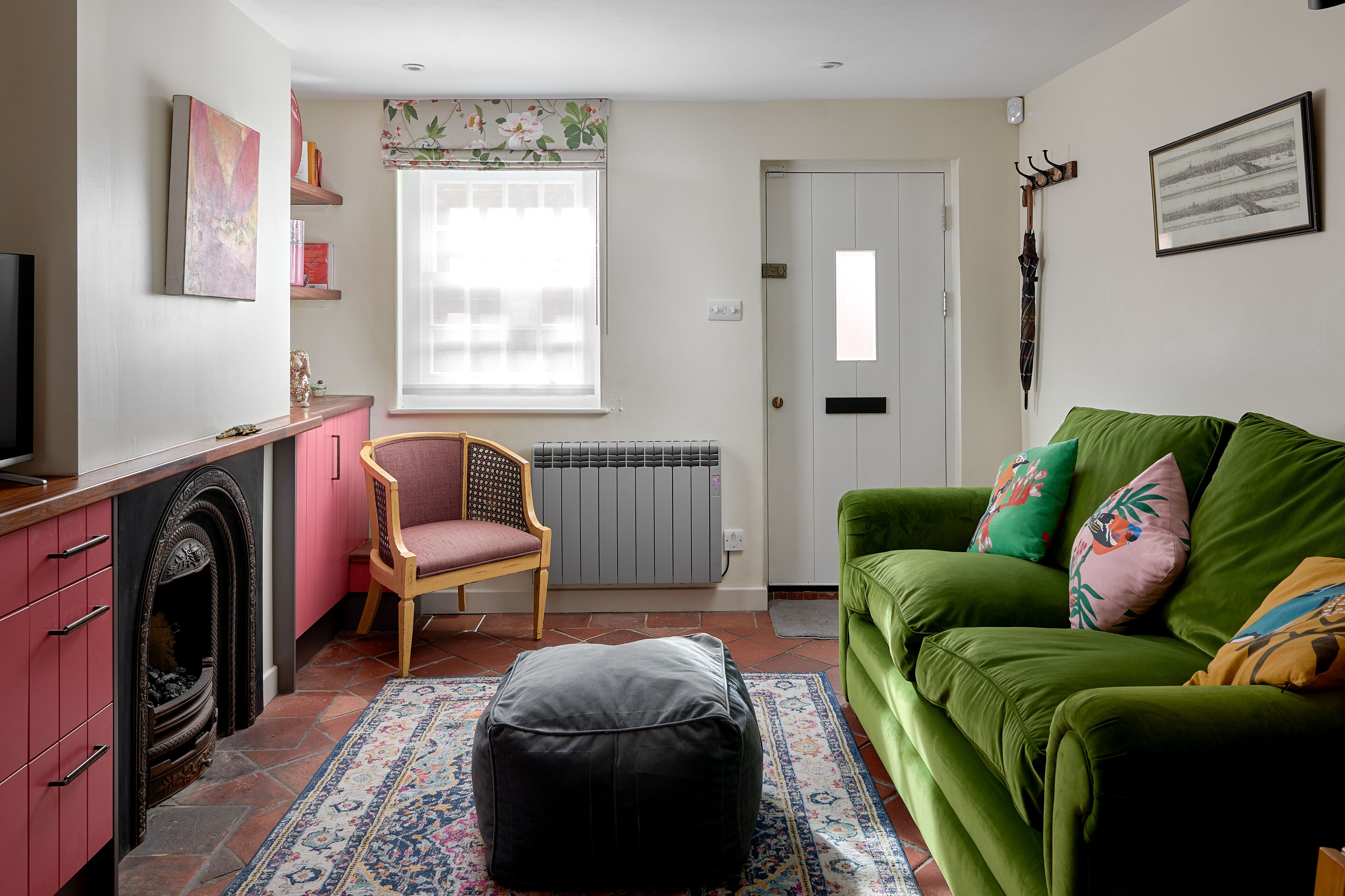 A cozy living room with a green sofa, a wooden chair, a black ottoman, a fireplace, and a radiator.