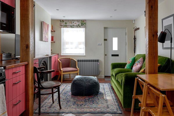 A compact living space with a kitchenette, a green sofa, a wooden table, and a patterned rug.