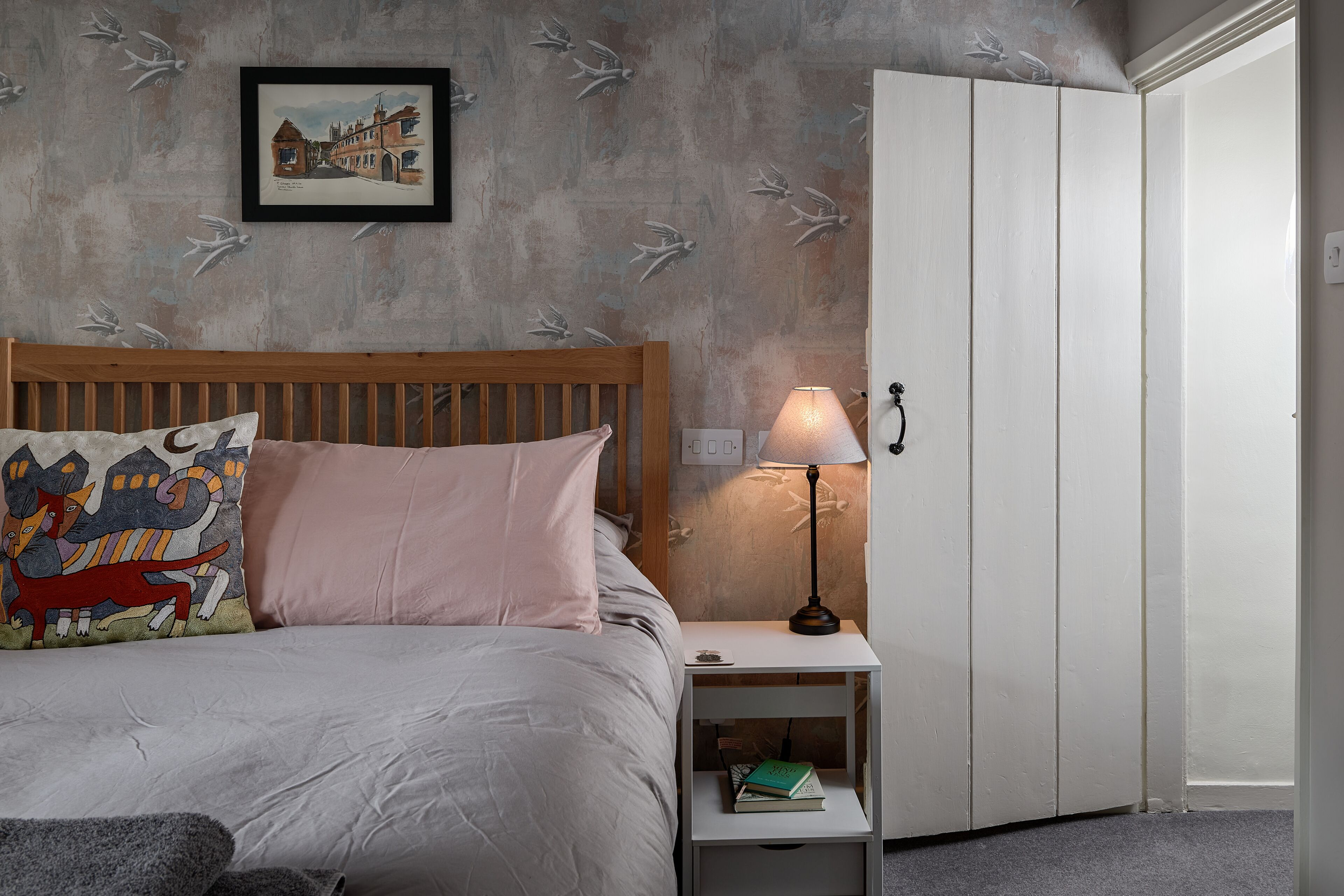 A bedroom with a bed, a nightstand with a lamp, a wardrobe, and a framed picture on the wall.