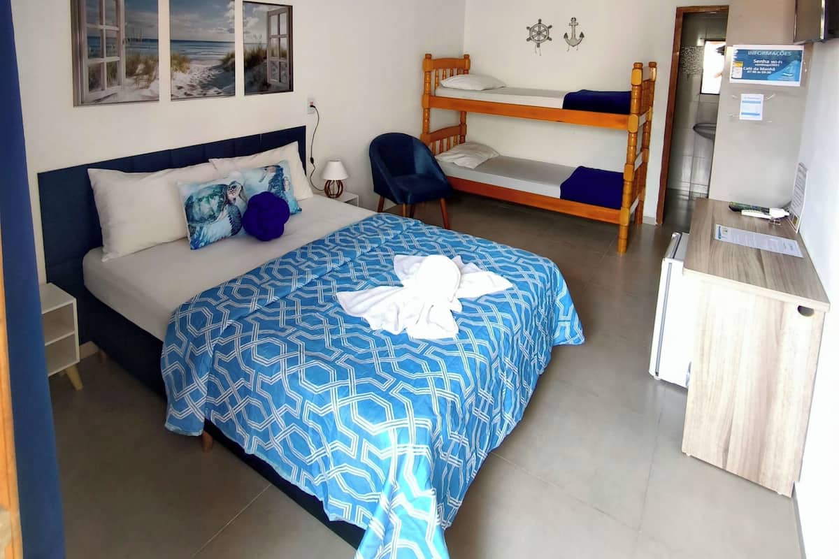 A hotel room with a bed, a desk, a chair, bunk beds, and a wall with three pictures.