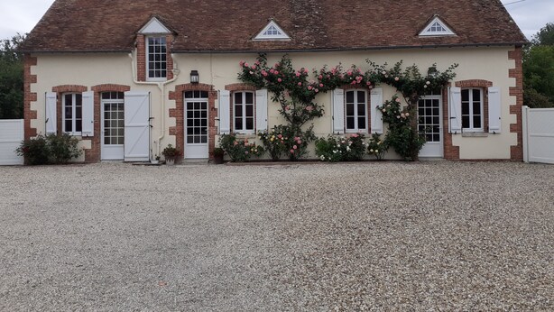 A two-story house with a tiled roof, white shutters, and a gravel driveway.