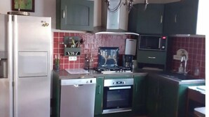 A compact kitchen with a refrigerator, stove, microwave, and green cabinets.