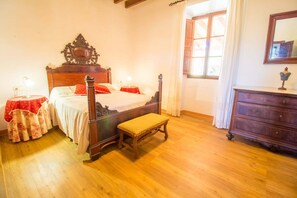 Une chambre à coucher de style traditionnel, avec un lit à baldaquin, un banc en bois, une commode et une fenêtre agrémentée de rideaux.
