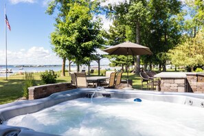 Un jacuzzi con caída de agua, rodeado de mobiliario exterior y una zona de patio con vistas al agua.