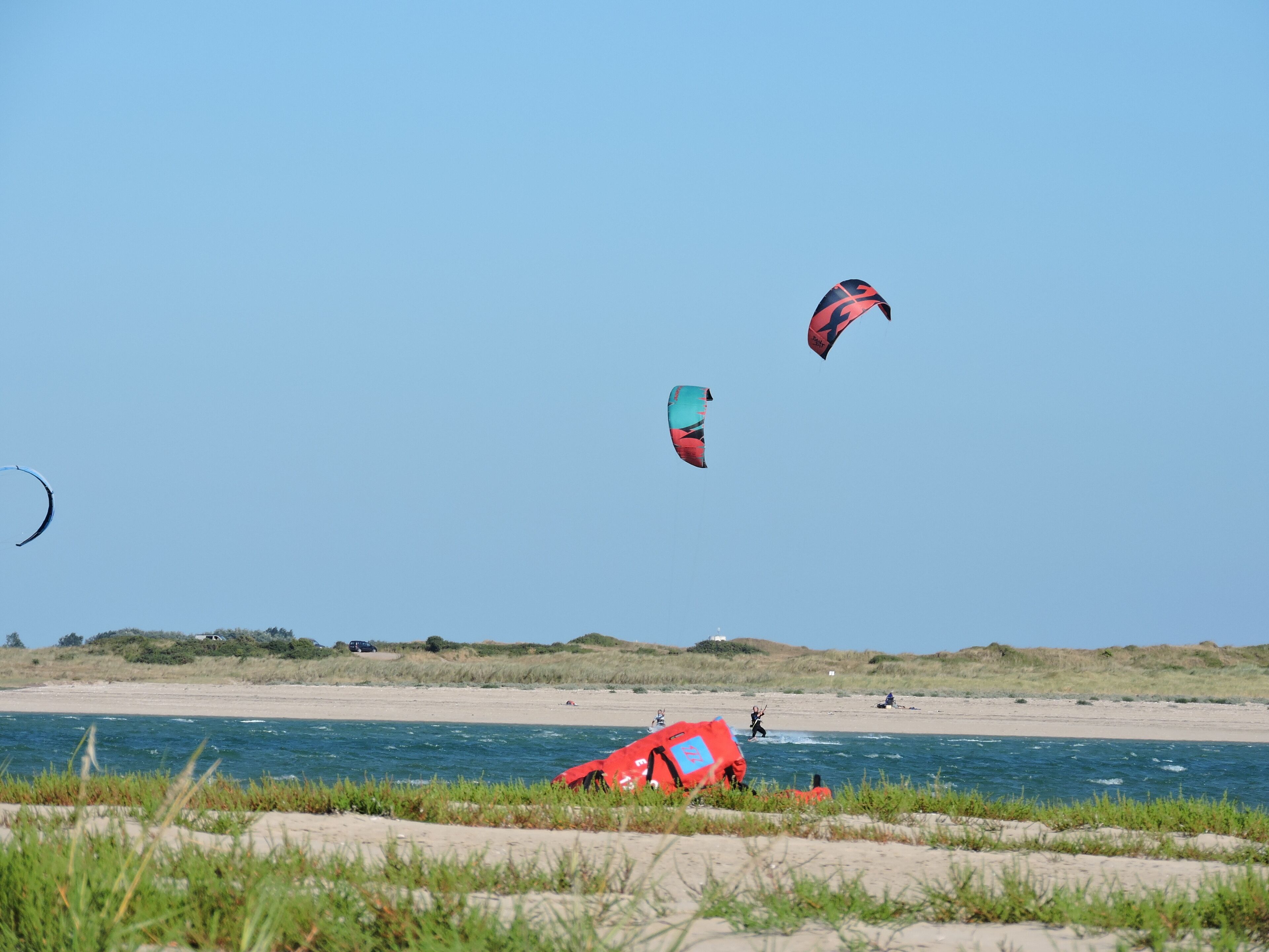 A beach with clear skies and three kites flying.