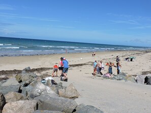 En strand med store sten i forgrunden og mennesker i baggrunden.