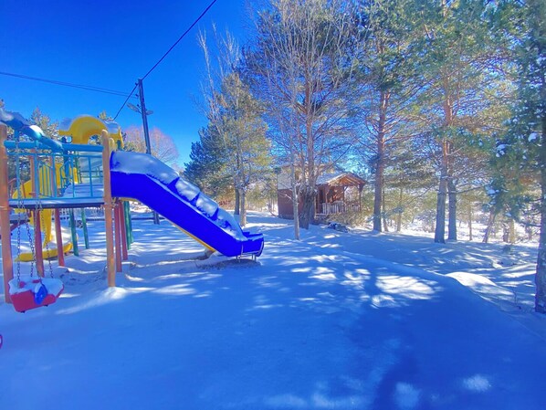 A snowy playground with a blue slide and a small cabin in the background. - Kibriscik Koroglu Dag Evleri (Kibriscik)