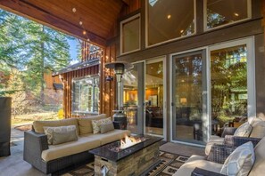 A modern outdoor living area with a stone fire pit, wicker furniture, and large sliding glass doors leading to an interior space. - Family Home, Hot Tub, Suncadia Pool Access (Cle Elum)