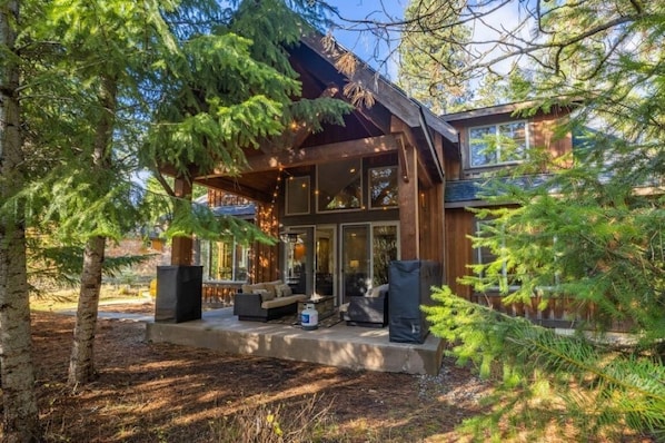 A modern log cabin with a covered porch, outdoor seating, and a fire pit.