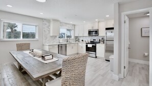 Una cocina moderna con armarios blancos, una mesa de comedor de madera y electrodomésticos integrados.