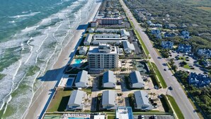 Vista aérea de un hotel costero con playa, varias edificaciones y una carretera paralela a la playa.