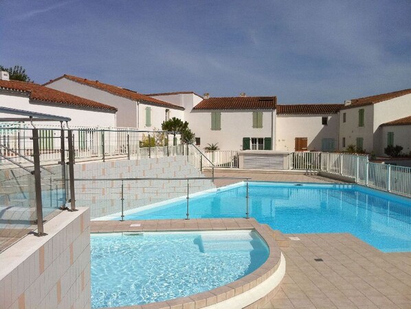A swimming pool with a tiled deck, surrounded by buildings with red-tiled roofs and white walls.