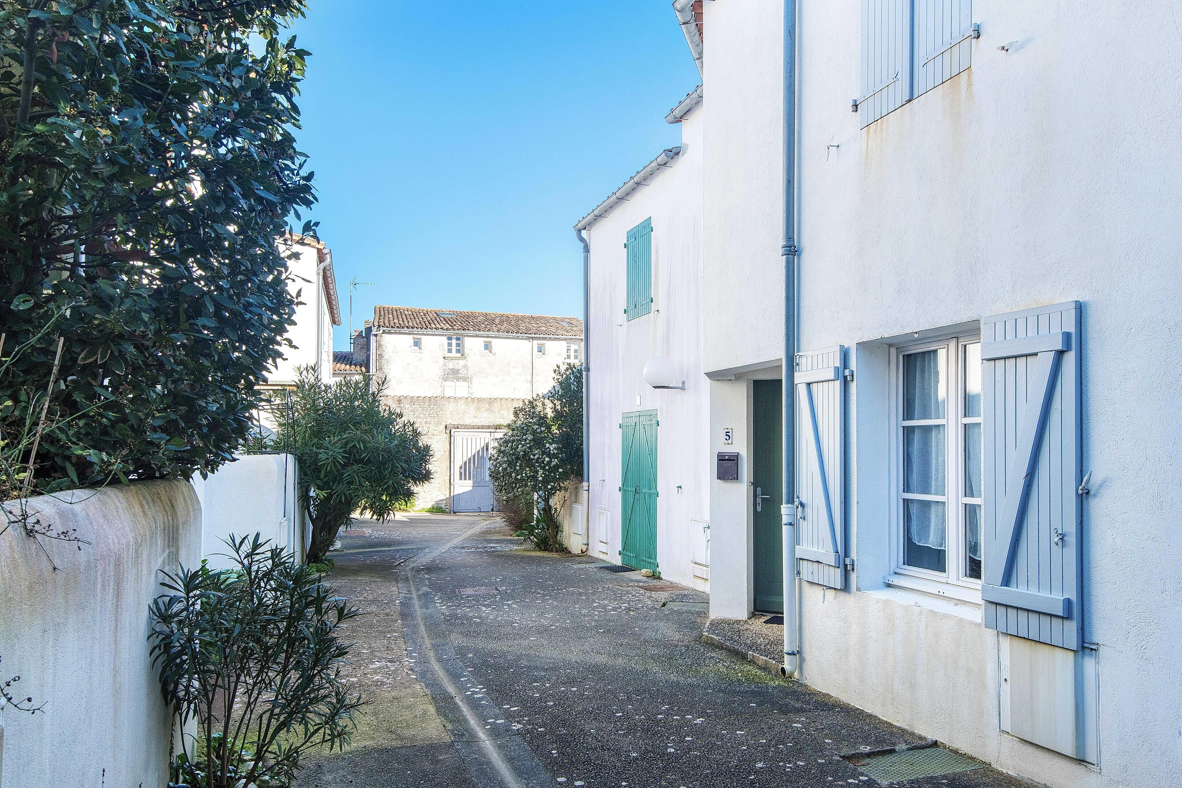 Une rue étroite bordée de bâtiments blancs, avec une porte verte et une plaque portant le numéro « 5 ».