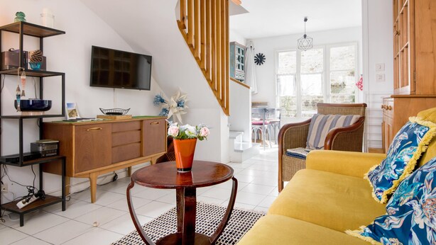 A modern living room with a staircase, a wooden cabinet, a television, and a yellow sofa. - Apartment SAINTE CLAIR (Saint-Martin-de-Ré)