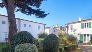A courtyard with white buildings, green shutters, and neatly trimmed hedges. - Apartment SAINTE CLAIR (Saint-Martin-de-Ré)