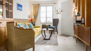 A room with a yellow sofa, wicker chair, and a small round table with a vase of flowers. - Apartment SAINTE CLAIR (Saint-Martin-de-Ré)