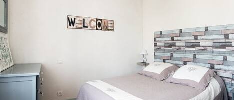 Een slaapkamer met een bed, een 'WELCOME' bord, een lamp en een dressoir.