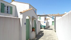 A narrow street with white buildings, green doors, and a clear blue sky.