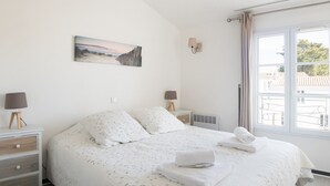 A bedroom with a bed, bedside tables, a lamp, a painting, and a window with curtains.