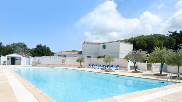 A swimming pool with blue water, surrounded by beige tiles. There are blue lounge chairs along the poolside.
