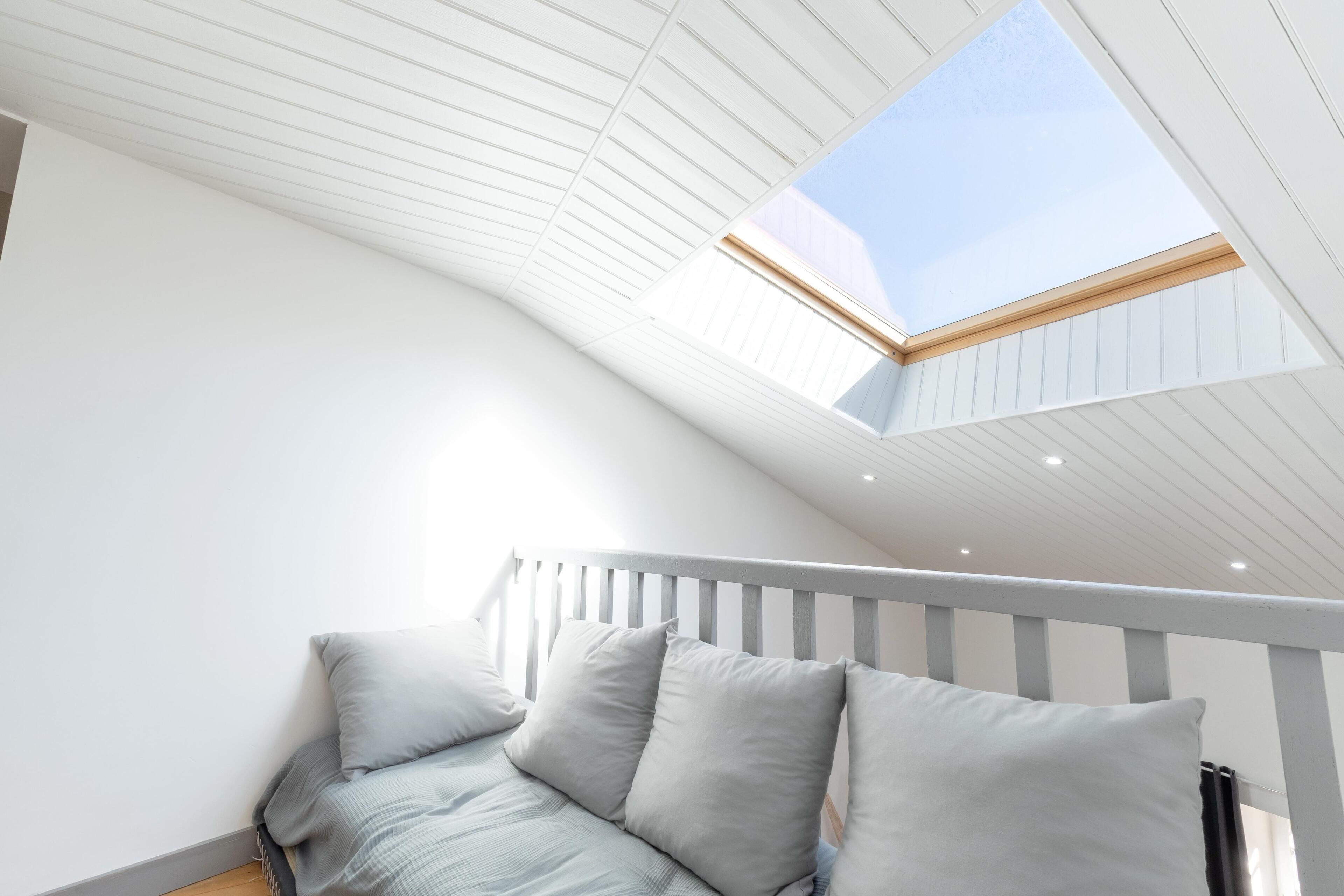 A room with a sloped ceiling, a skylight, a white railing, and a bed with pillows.