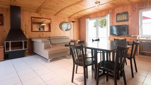 Ein Holzinnenraum mit einer Couch, einem Esstisch, Stühlen, einem Kamin, einem Fernseher und einer Küchenzeile.