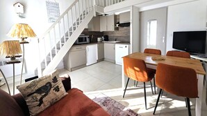A modern kitchen with white cabinets, a dining area with orange chairs, a staircase, and a flat-screen TV.